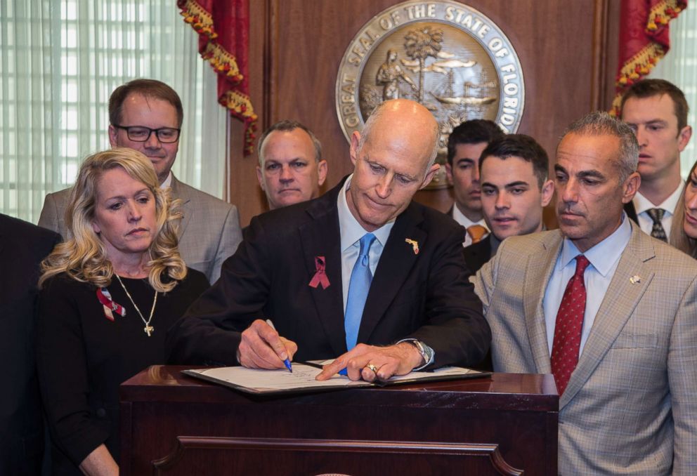 PHOTO: Florida Gov. Rick Scott signs the Marjory Stoneman Douglas Public Safety Act in the governor's office at the Florida State Capitol in Tallahassee, March 9, 2018. Scott is flanked by some of the parent's of the victims.