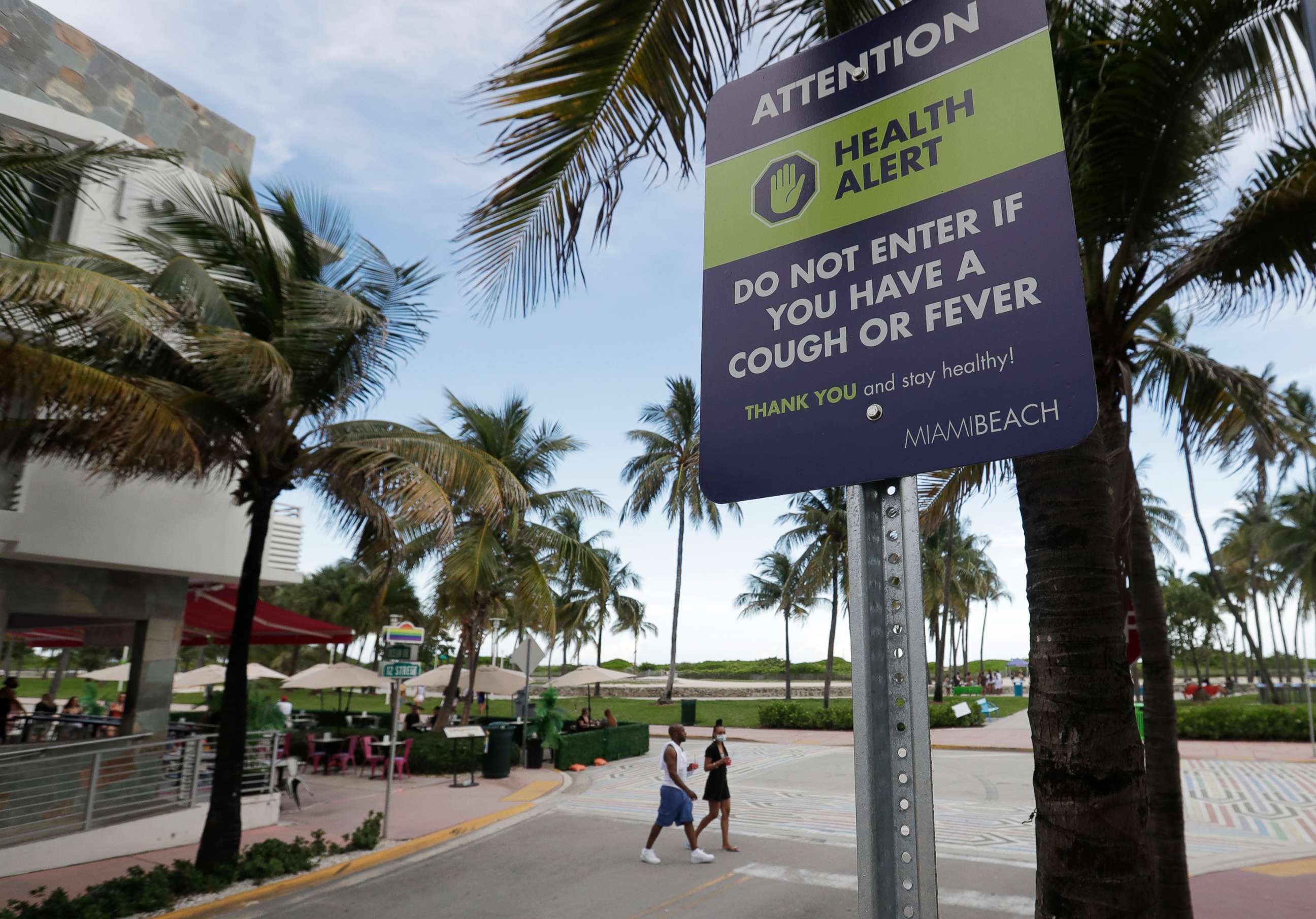 PHOTO: A couple walks past a sign asking people not to visit Miami Beach, Florida's famed South Beach if they have a cough or fever, June 22, 2020.