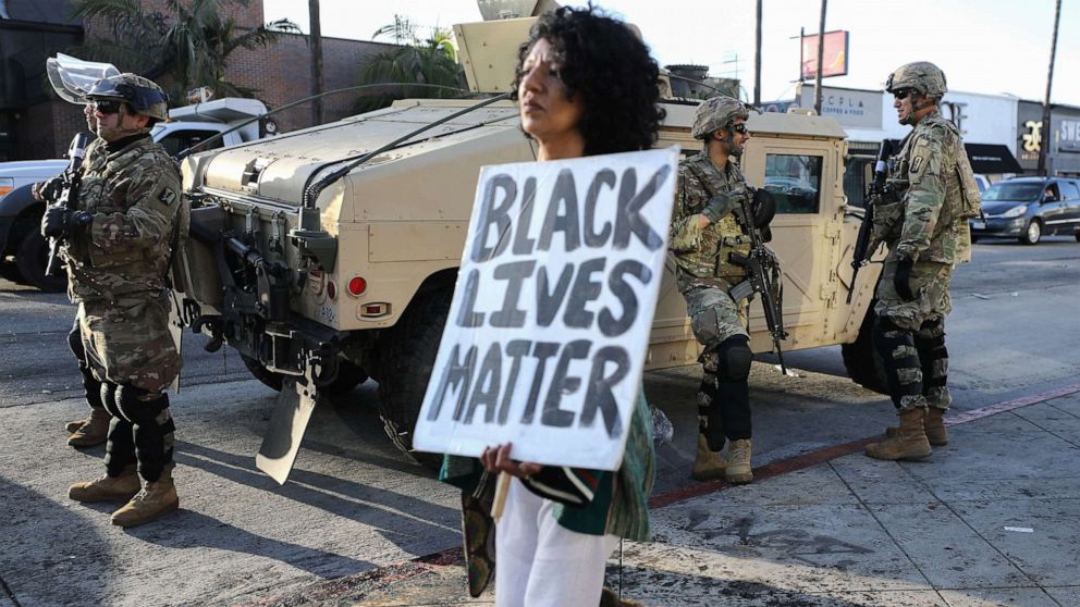 PHOTO: A woman carries a 'Black Lives Matter' sign past U.S. National Guard troops, May 31, 2020, in Los Angeles.