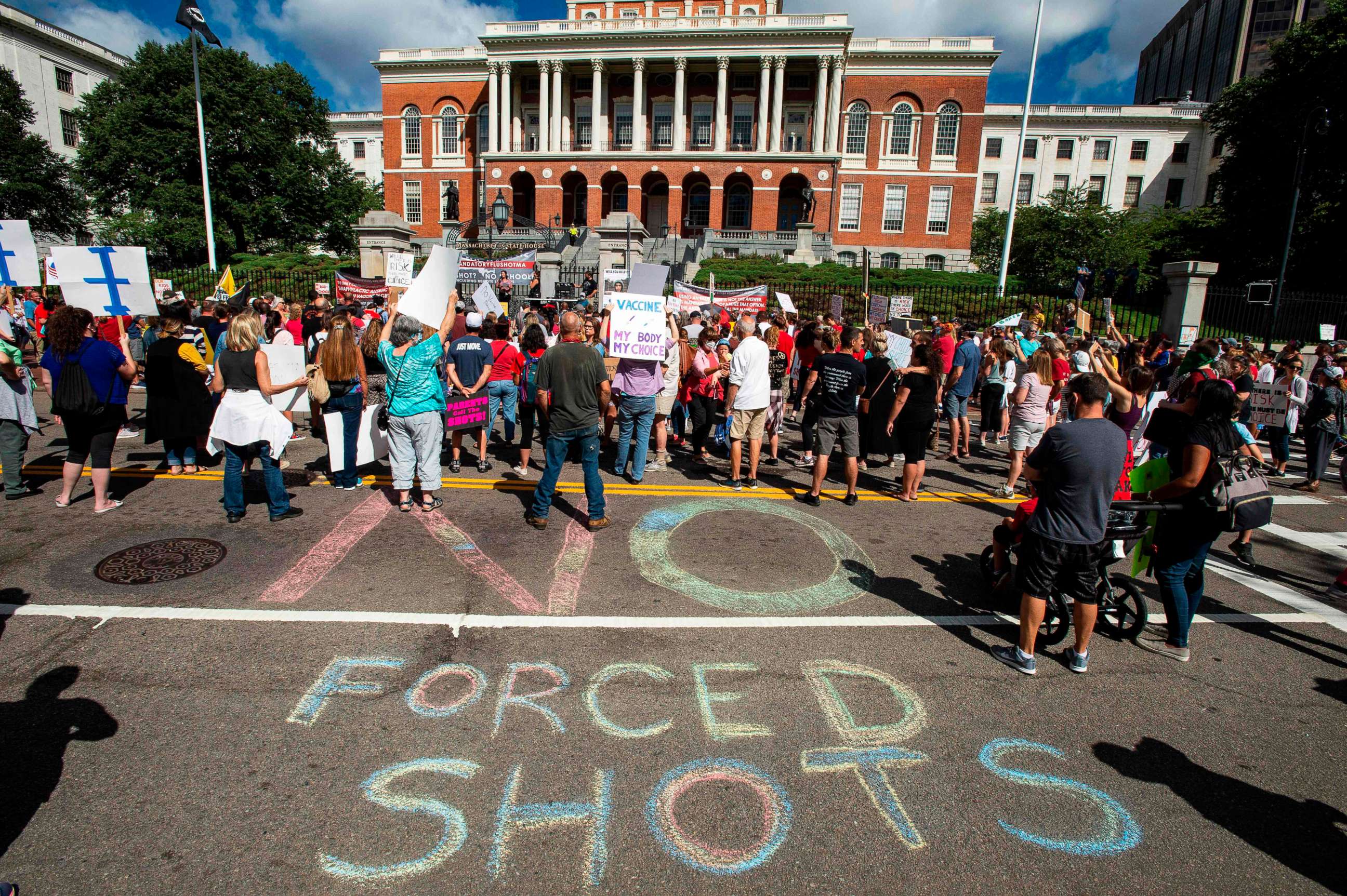 PHOTO: People draw a "No Forced Shots" message on the street in chalk  during a protest after a mandate requiring all children,age K-12, to receive an influenza (flu) vaccine/shot to attend school in Boston on August 30, 2020. 