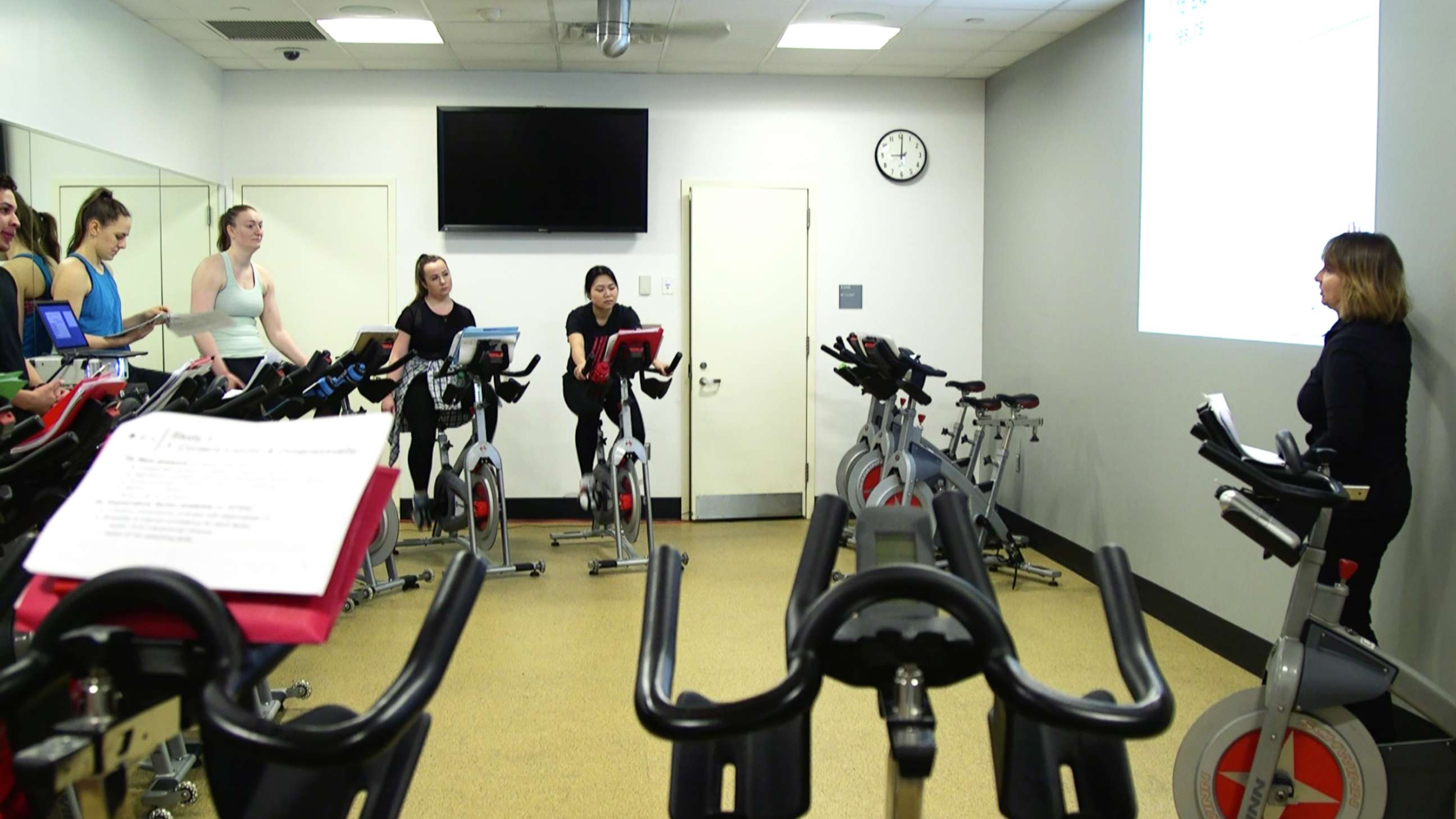 PHOTO: Fordham University professor Julita Haber teaches a business course while students are on spin bikes.