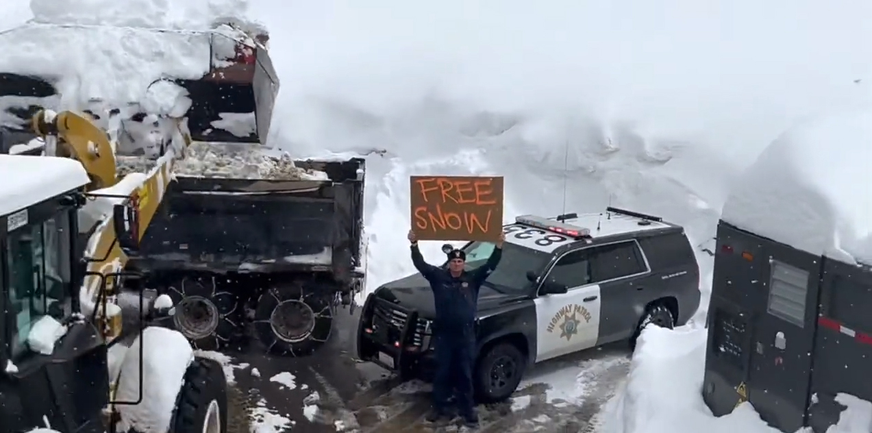 PHOTO: In this screen grab from a video posted on March 3, 2023, to the CHP Truckee Twitter account, an officer holds up a "Free Snow" sign as a truck removes snow from the area in Truckee, Calif.