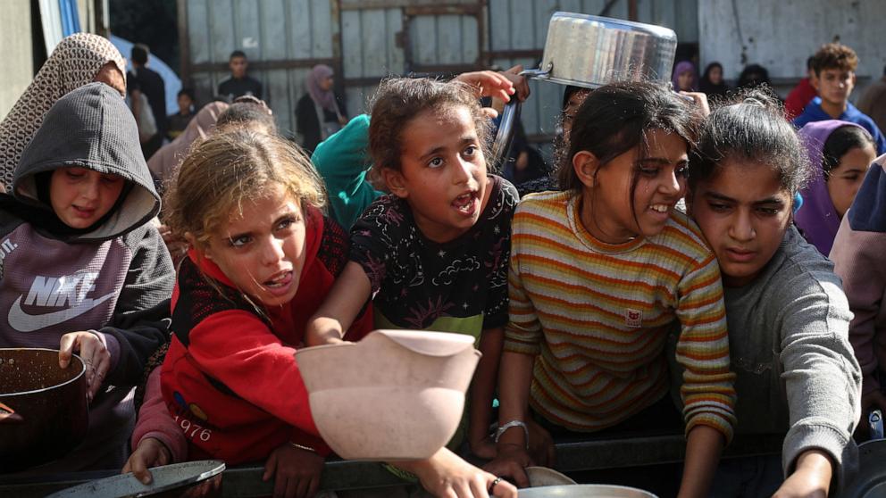 PHOTO: Displaced Palestinians, children and adults, wait for a food portion at a shelter where families have been living, in Nuseirat, in the central of Gaza Strip, November 23, 2025. 