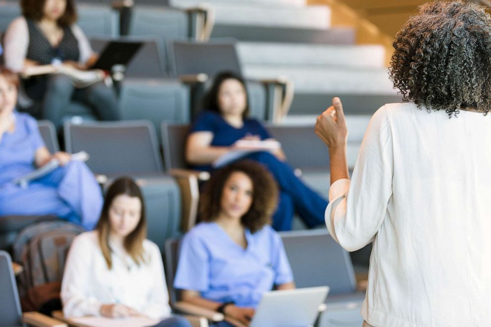 STOCK PHOTO: A teacher gestures as she lectures a class of college students.