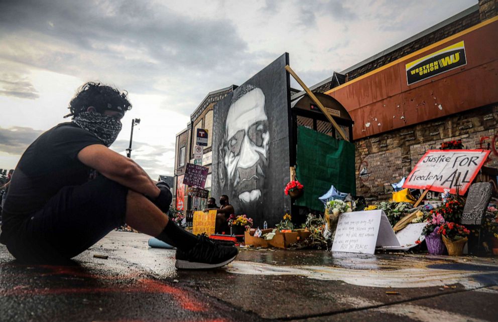 PHOTO: After a new mural, center, of George Floyd is added to a growing memorial of tributes, Trevor Rodriquez sits alone at the spot where Floyd died while in police custody, Tuesday June 2, 2020, in Minneapolis.