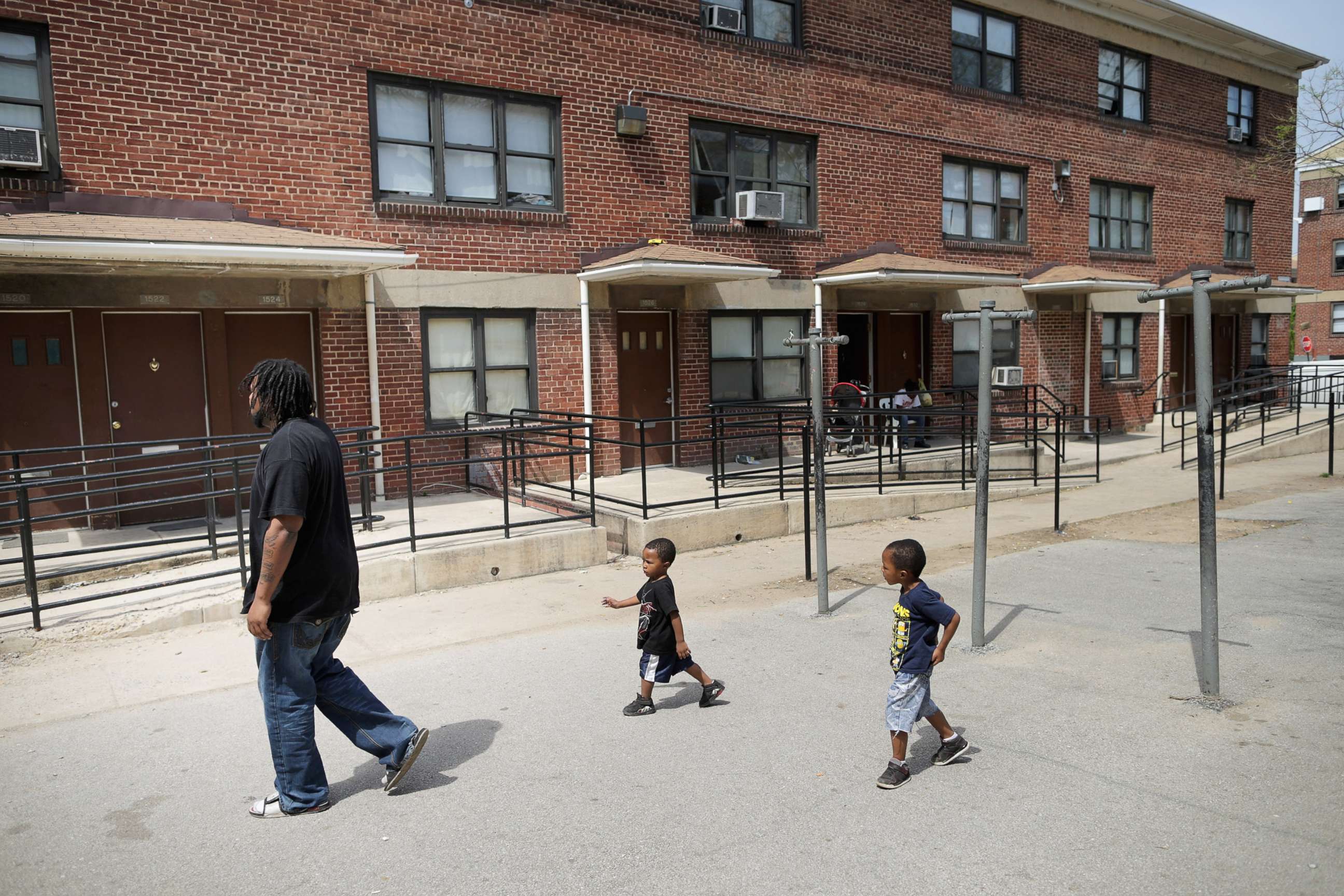 PHOTO: A man walks through the courtyard outside his apartment in the Gilmor Homes with two of his six children, one year after Freddie Gray died, April 19, 2016, in Baltimore.