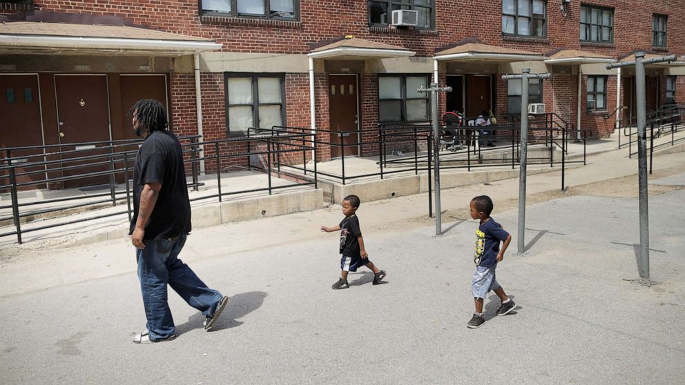 PHOTO: A man walks through the courtyard outside his apartment in the Gilmor Homes with two of his six children, one year after Freddie Gray died, April 19, 2016, in Baltimore.