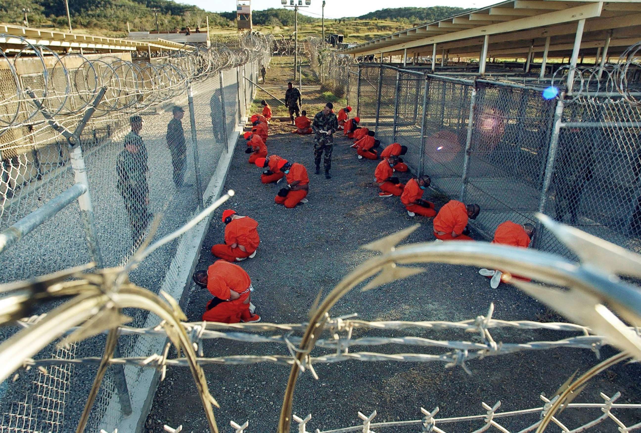 PHOTO: Detainees in orange jumpsuits sit in a holding area under the watch of U.S. military police at Camp X-Ray at Naval Base Guantanamo Bay, Cuba, during in-processing to the temporary detention facility, Jan. 11, 2002. 
