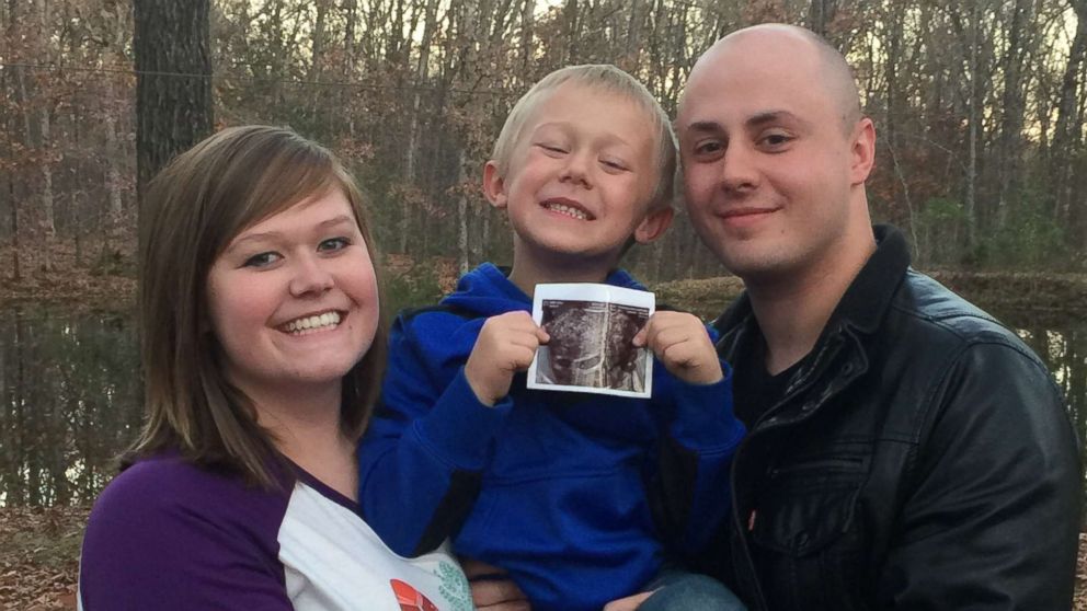 Micaela Johnson, with her husband and son, who is holding a sonogram photo of her twins. Johnson's mother is serving as her surrogate.