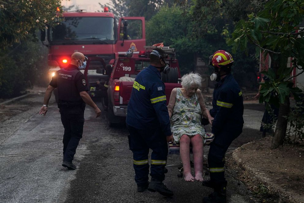 PHOTO: Firefighters evacuate an elderly woman from her house in Penteli, Greece, July 19, 2022. Hundreds of people were ordered to leave their homes after a large forest fire broke out northeast of Athens.