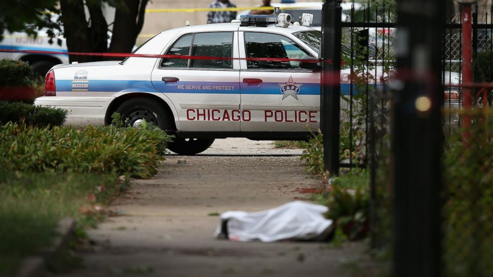 Police investigate the shooting death of 14-year-old Tommy McNeal, whose body is covered by a sheet on the sidewalk on September 20, 2013 in Chicago, Illinois.