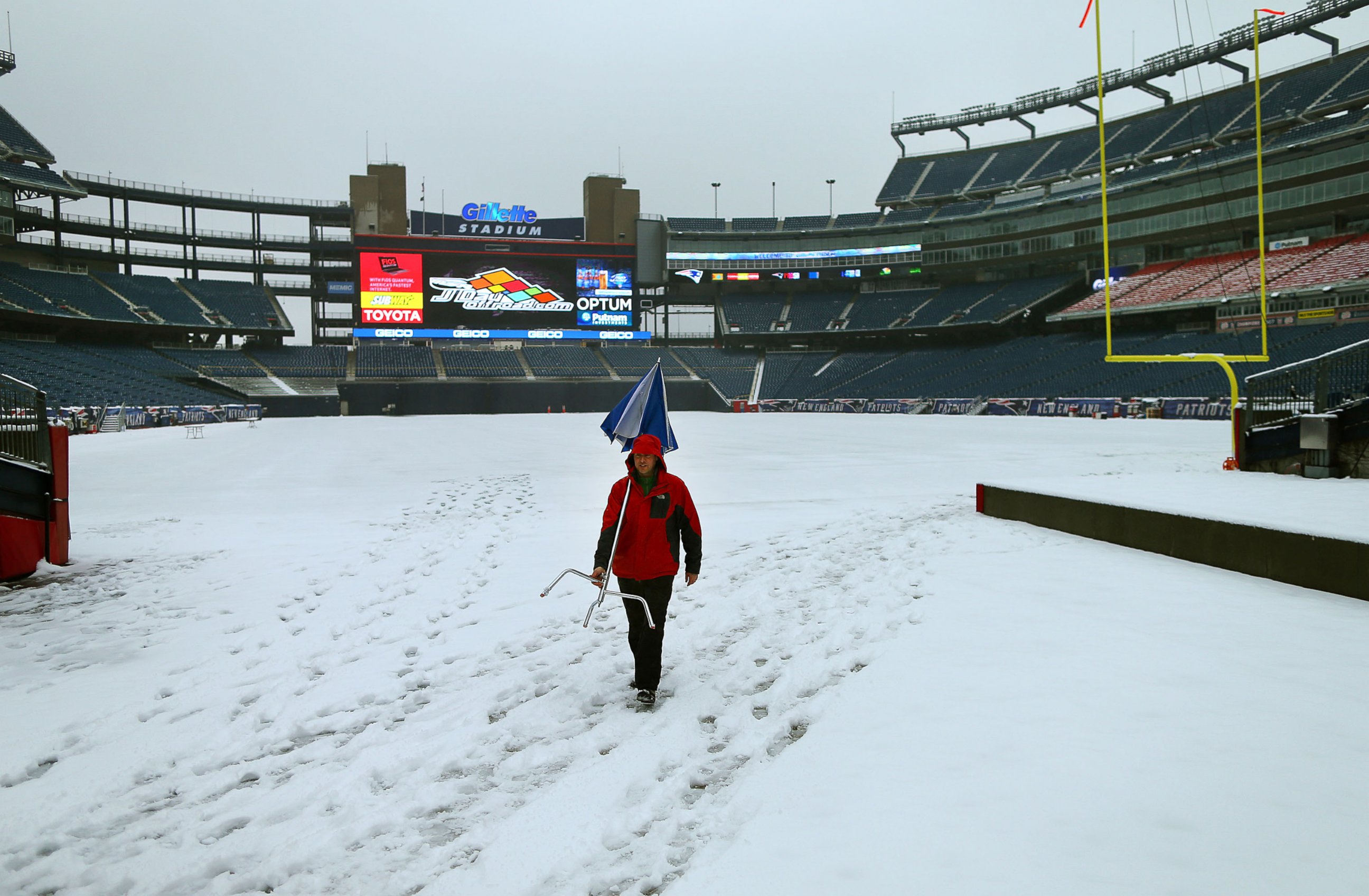 PHOTO:  Snow covers the field at Gillette Stadium as a tv crew member walks by with an umbrella and stand, on Jan. 24, 2015.