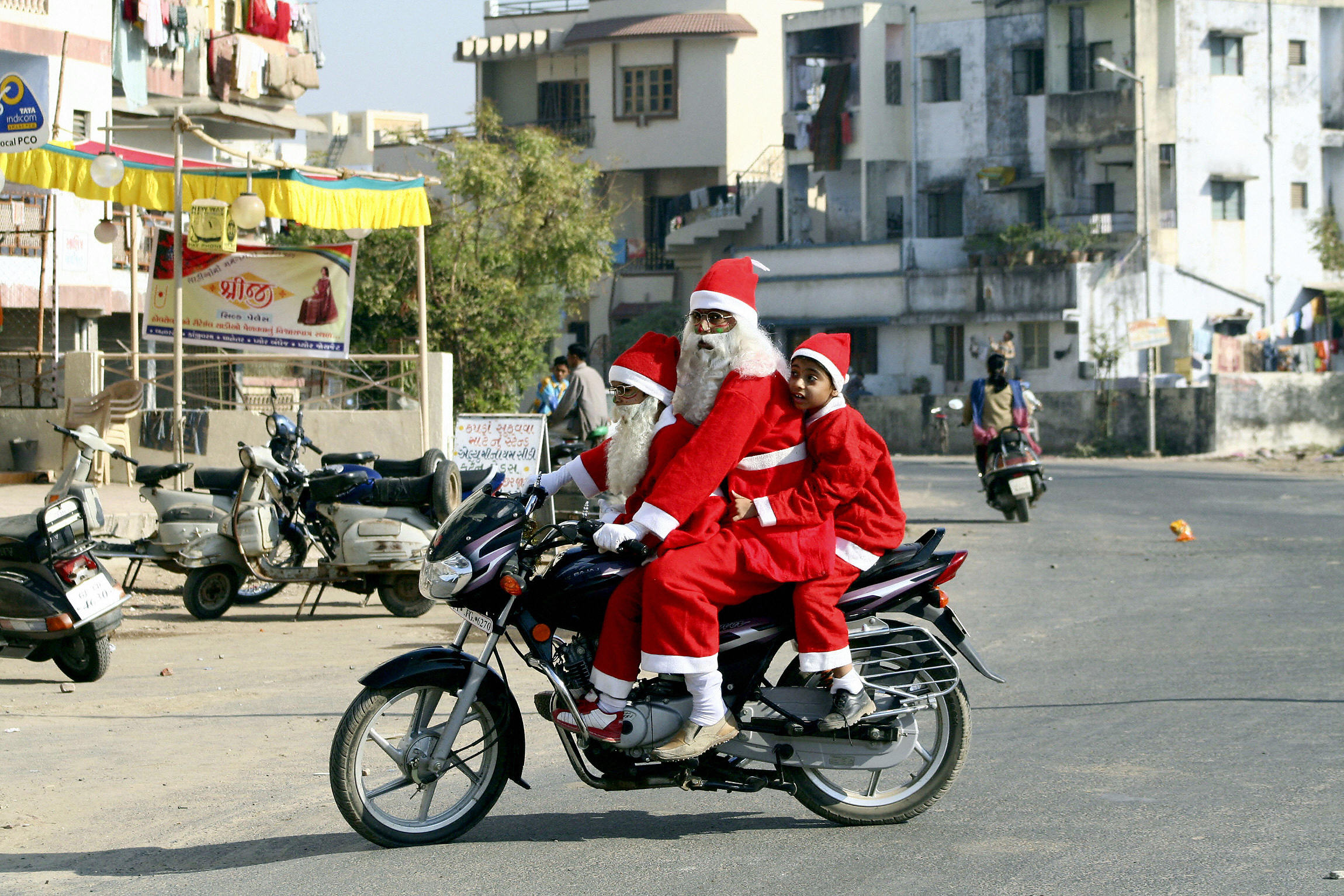 PHOTO: An Indian man and a pair of children dressed as Santa Claus ride a motorcycle along a street of Ahmedabad, December 21, 2006. 