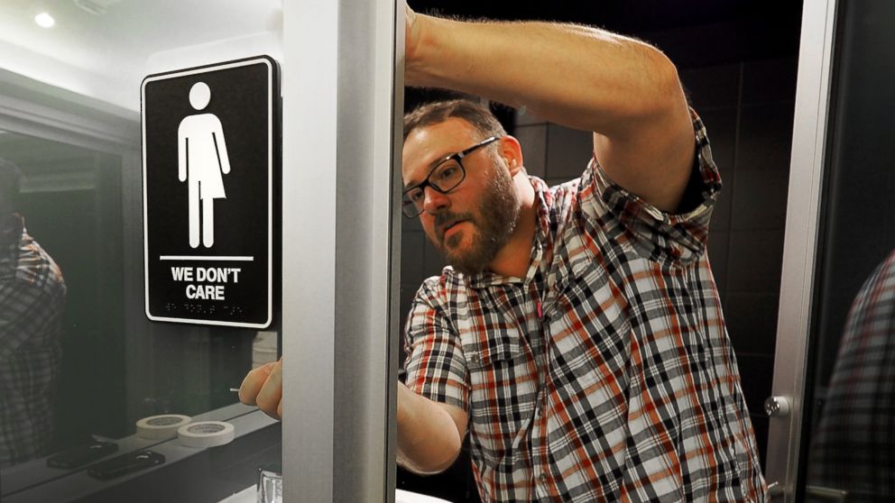 Museum manager Jeff Bell adheres informative backing to gender neutral signs in the 21C Museum Hotel public restrooms on May 10, 2016 in Durham, N.C.