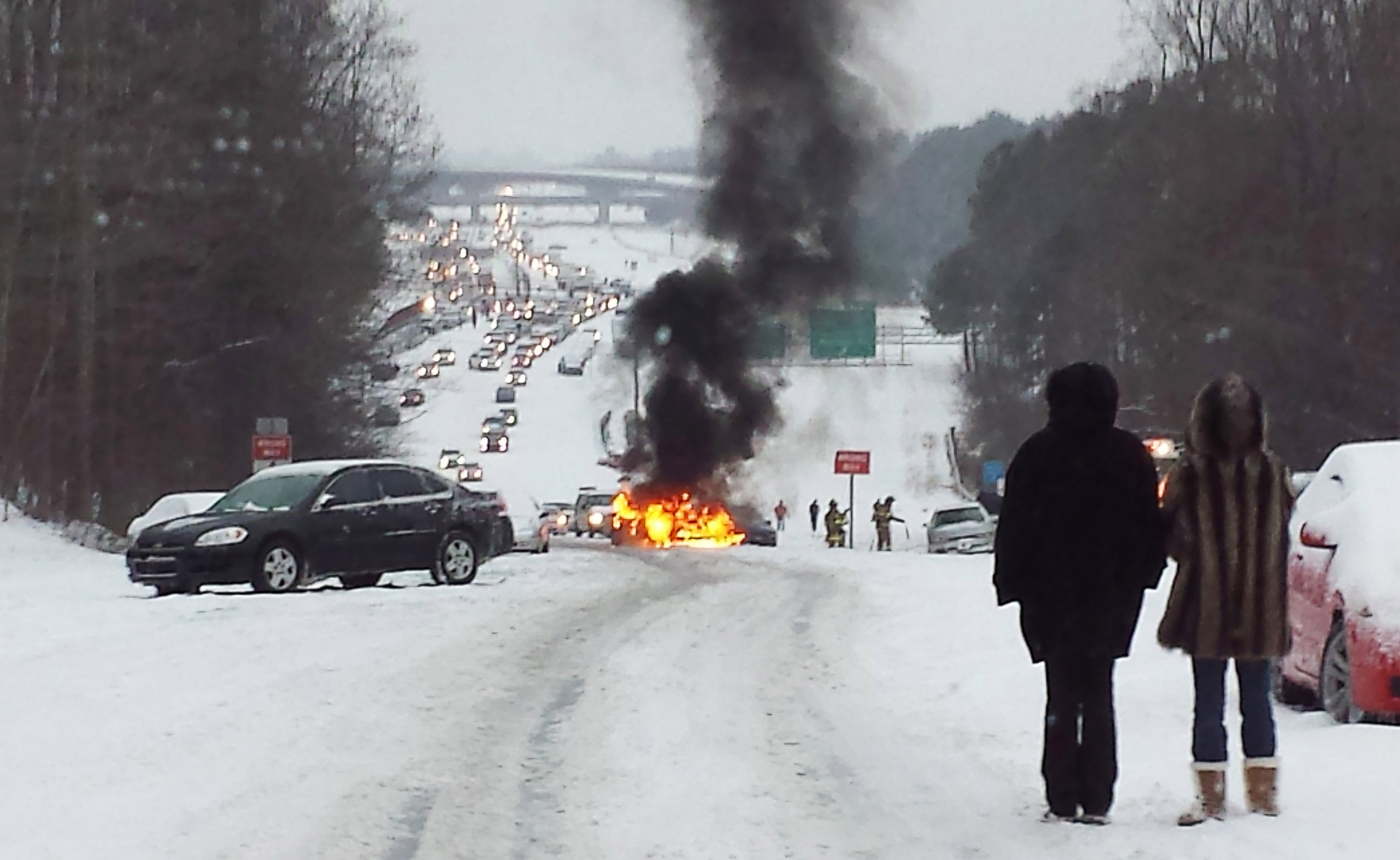 PHOTO: Motorists watch a vehicle burn after it caught fire while struggling to get up a snow covered hill in Raleigh, North Carolina on February 12, 2014.