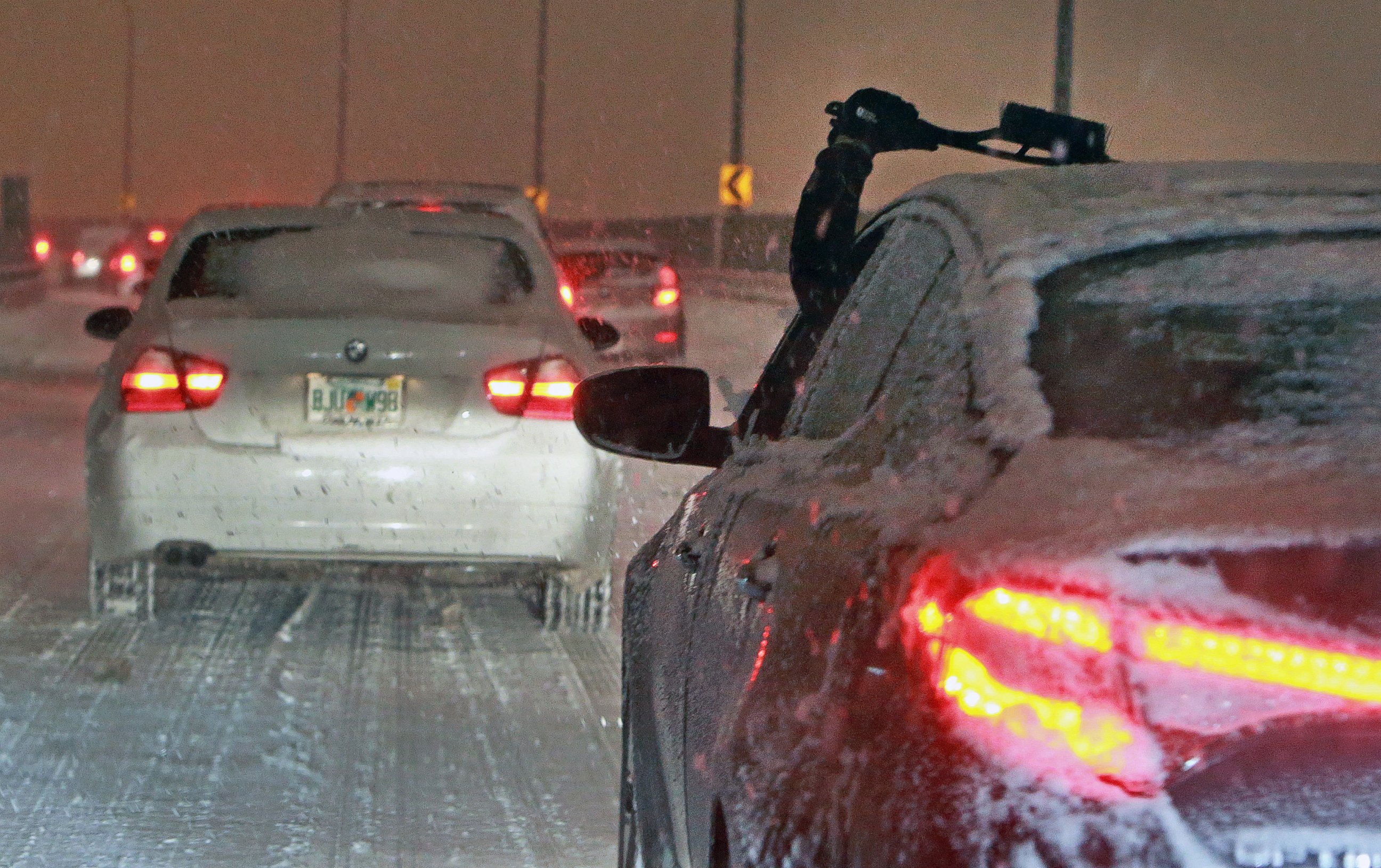 A driver reaches out to clear their windshield of snow and ice while navigating storm snarled traffic in Boston on Dec. 17, 2013.