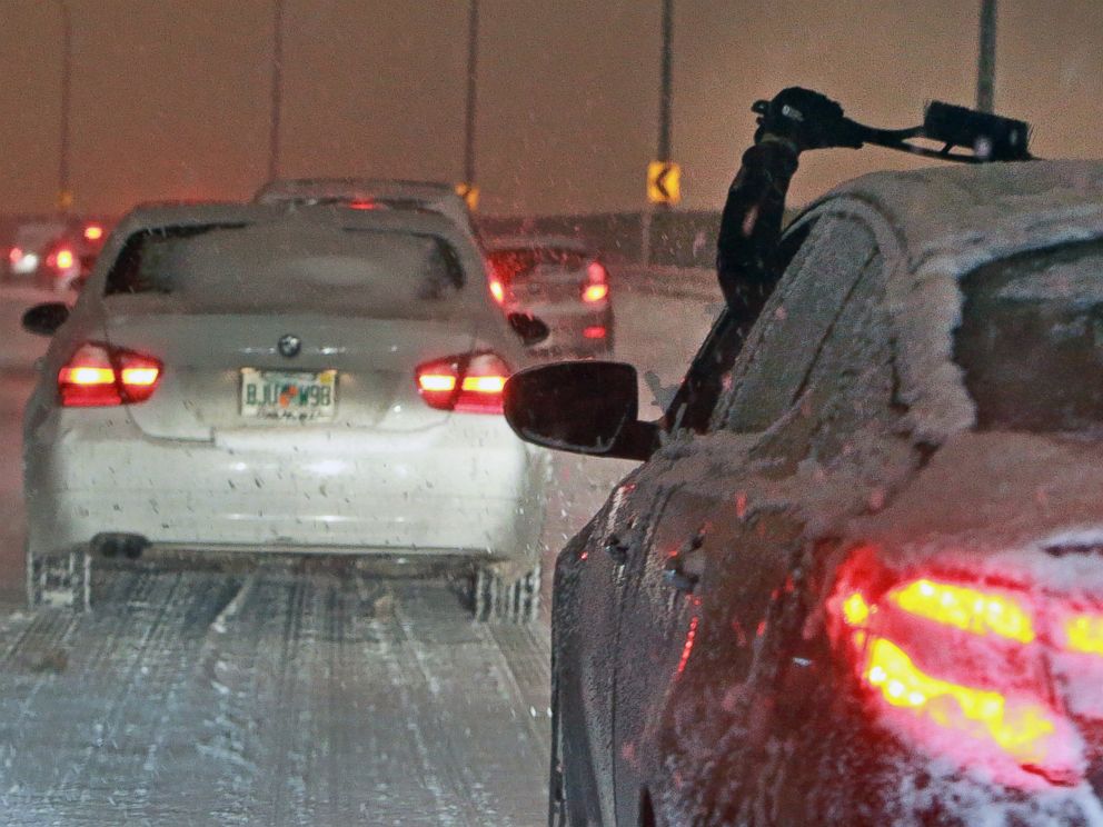 A driver reaches out to clear their windshield of snow and ice while navigating storm snarled traffic in Boston on Dec. 17, 2013.
