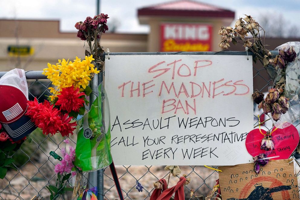 PHOTO: FILE - In this April 23, 2021, file photo, a sign hangs amid the tributes that cover the temporary fence around the King Soopers grocery store in which 10 people died in a mass shooting in late March in Boulder, Colo. 