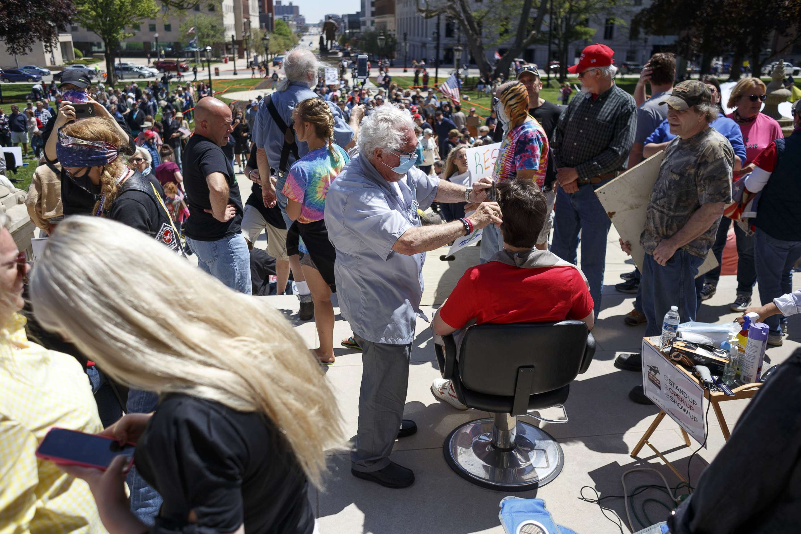 PHOTO: Owosso barber, Karl Manke, gives a free haircut to Parker Shonts, of Lake Orion, on the steps of the state Capitol during Operation Haircut on May 20, 2020 in Lansing, Michigan.