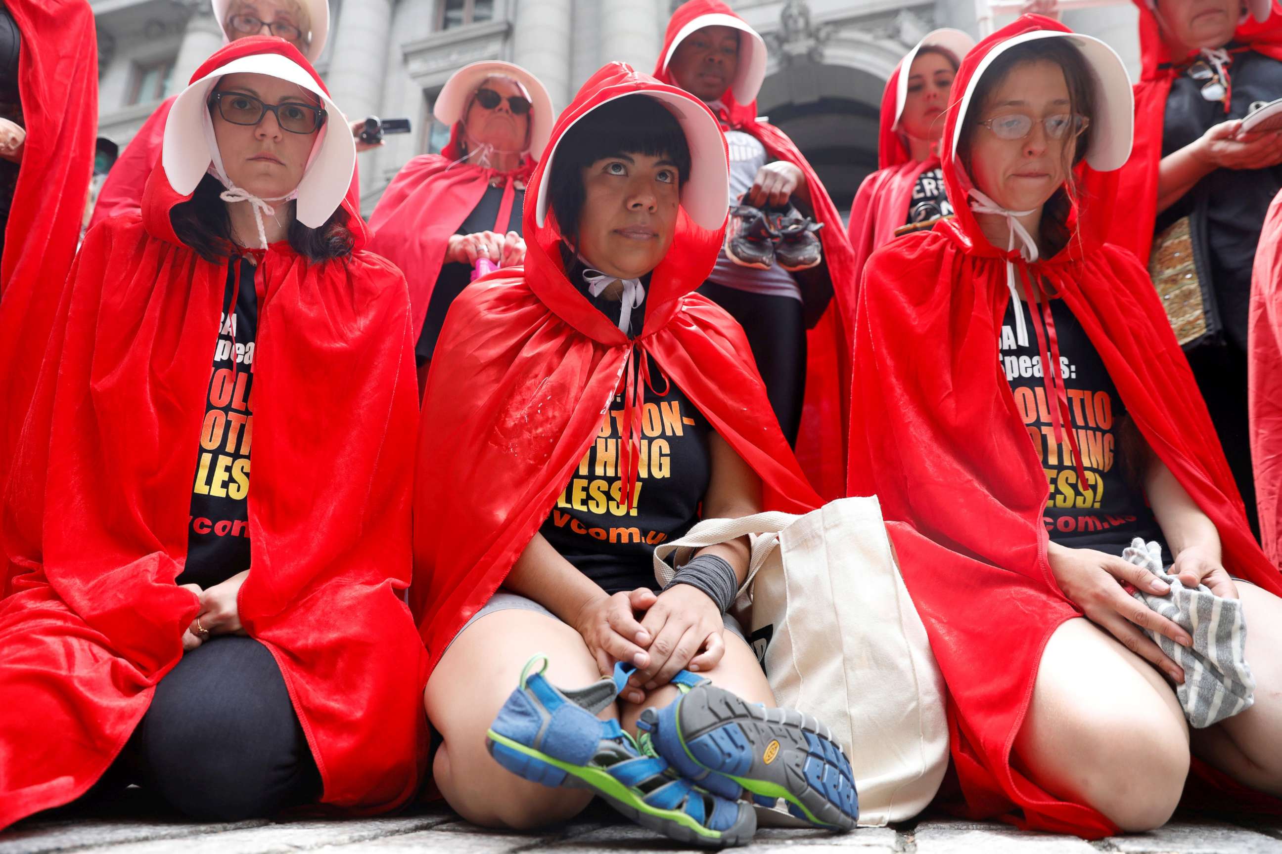 PHOTO: Women dressed in red gowns as worn in the "Handmaids Tale" hold shoes and clothing representing immigrant children separated from their parents as they protest in New York City, July 31, 2018.