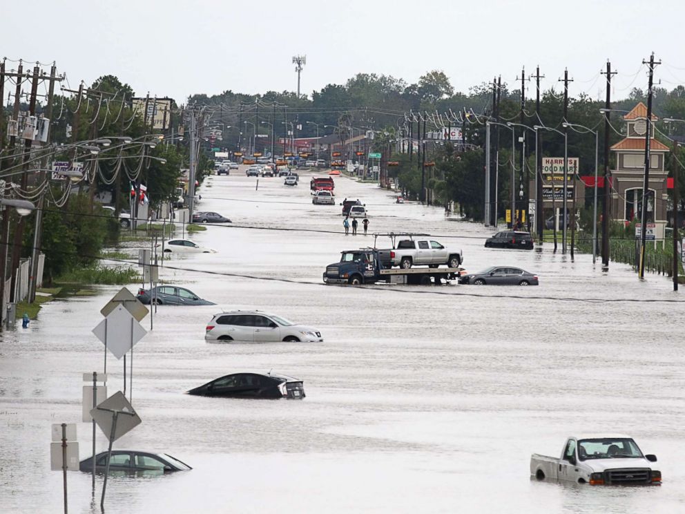 PHOTO: A car gets towed while men walk in the flooded waters of Telephone Rd. in Houston, Texas on Aug. 30, 2017.
