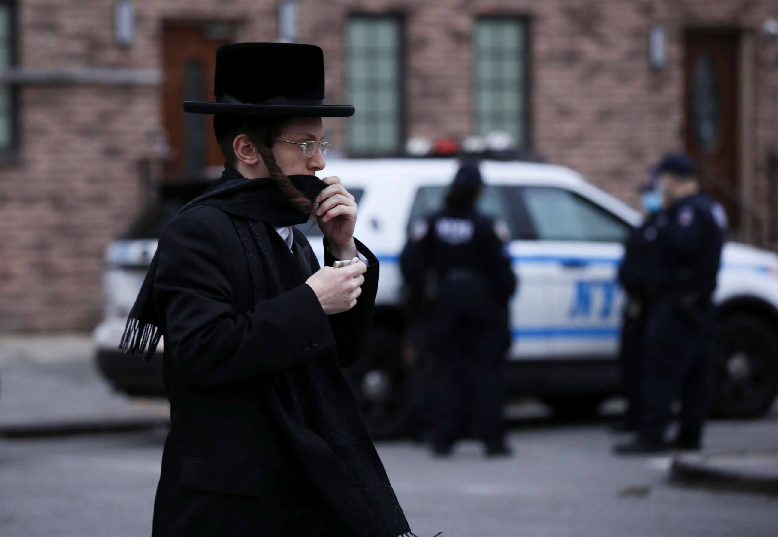 PHOTO: A man moves his scarf to cover his face as he passes NYPD officials stationed in the Orthodox Jewish community of the Williamsburg neighborhood during the outbreak of the coronavirus disease (COVID19) in New York, April 30, 2020.