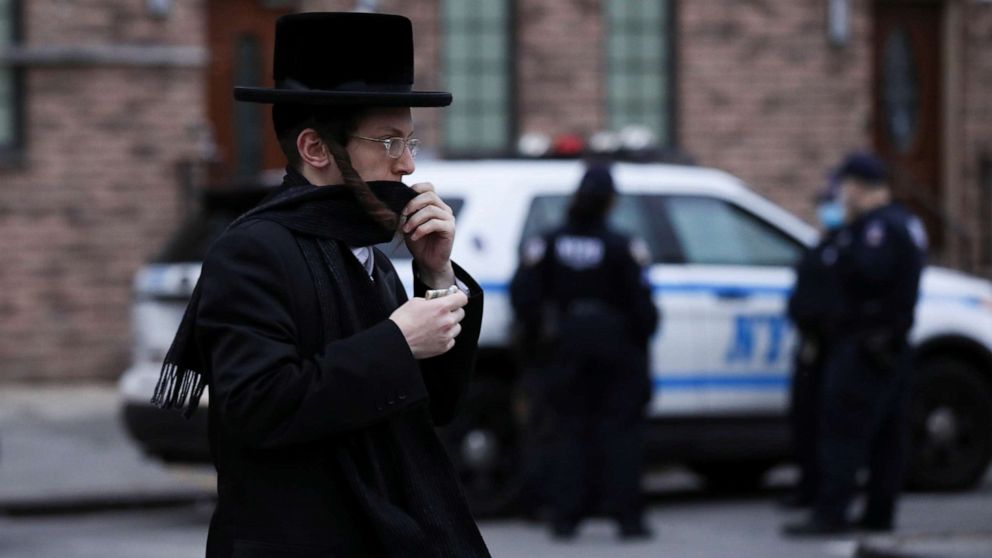 PHOTO: A man moves his scarf to cover his face as he passes NYPD officials stationed in the Orthodox Jewish community of the Williamsburg neighborhood during the outbreak of the coronavirus disease (COVID19) in New York, April 30, 2020.