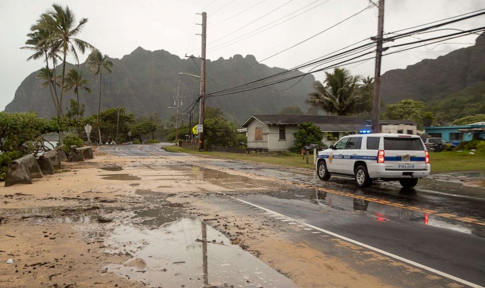 PHOTO: A police officer with the Honolulu Police Department inspects the sand and debris washed onto a closed portion of Kamehameha Highway, July 26, 2020, in Kaaawa, Hawaii.