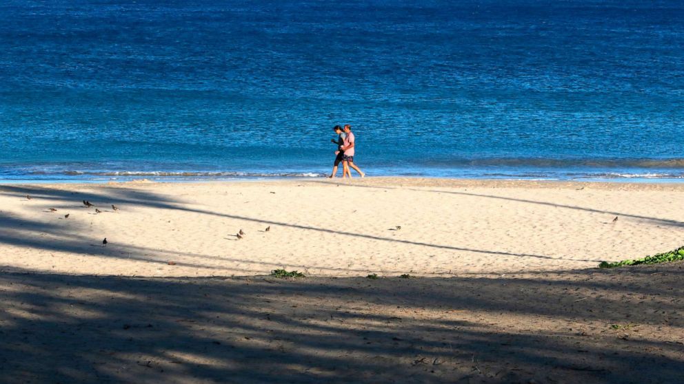 PHOTO: A couple walks on a beach near Waimea, Hawaii, on Friday, Aug. 6, 2021. The area was scorched by the state's largest ever wildfire. 