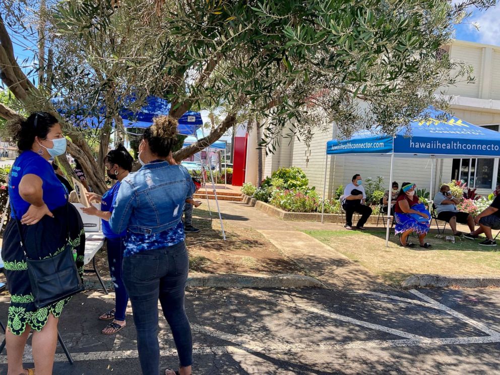 PHOTO: In this July 14, 2021, file photo, members of the community group We are Oceania, get ready to start a COVID-19 vaccination clinic as people wait for it to start in Honolulu.