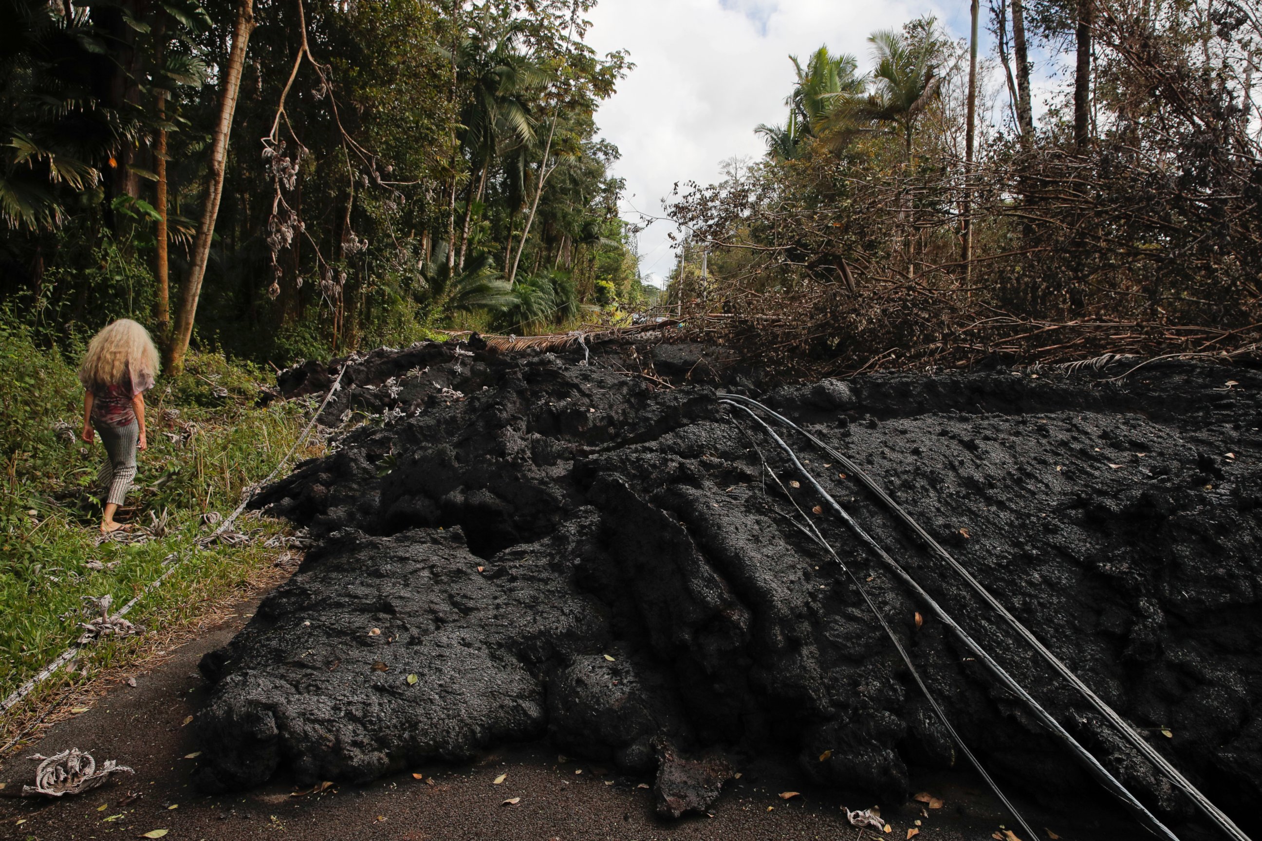 Hannique Ruder, a 65-year-old resident living in the Leilani Estates subdivision, walks past the mound of hardened lava while surveying the neighborhood Friday, May 11, 2018, near Pahoa, Hawaii.