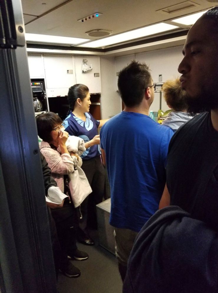 This Friday, Aug. 31, 2018 photo provided by Nicholas Andrade shows people gathered in a back galley on a Hawaiian Airlines flight from Oakland, Calif., to Kahului, Hawaii, after a can of pepper spray went off inside the plane.