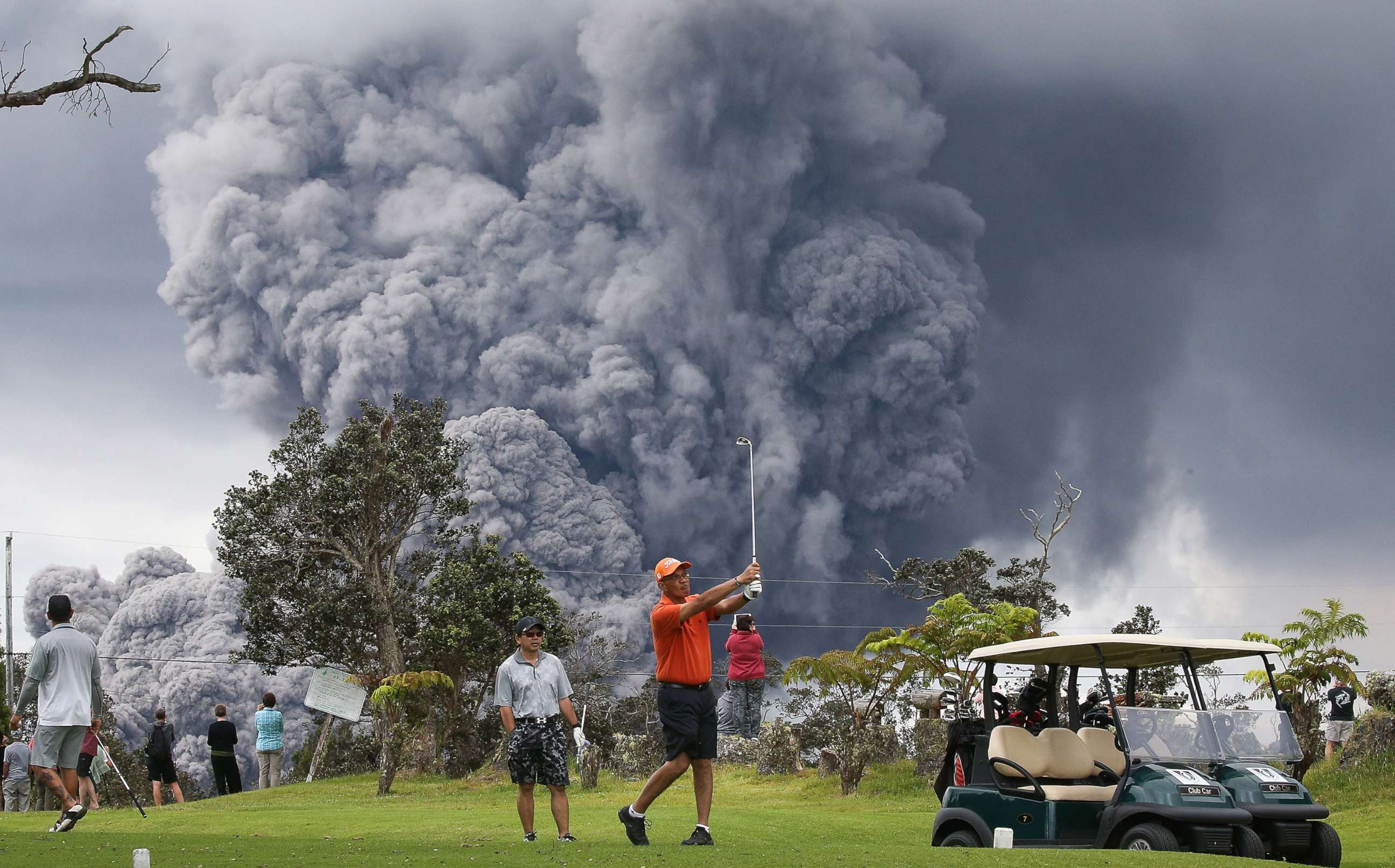 PHOTO: People play golf as an ash plume rises in the distance from the Kilauea volcano on Hawaii's Big Island, May 15, 2018, in Hawaii Volcanoes National Park, Hawaii. 