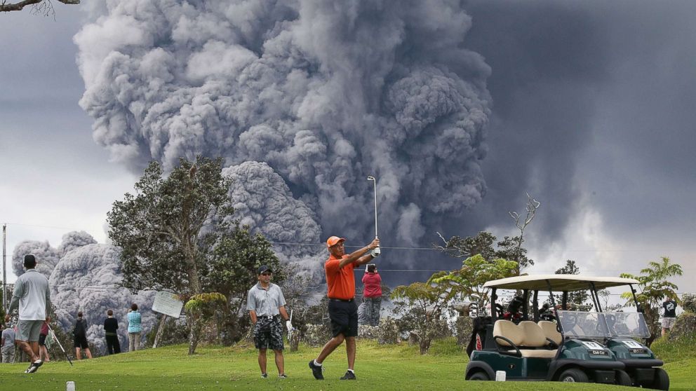 PHOTO: People play golf as an ash plume rises in the distance from the Kilauea volcano on Hawaii's Big Island, May 15, 2018, in Hawaii Volcanoes National Park, Hawaii.