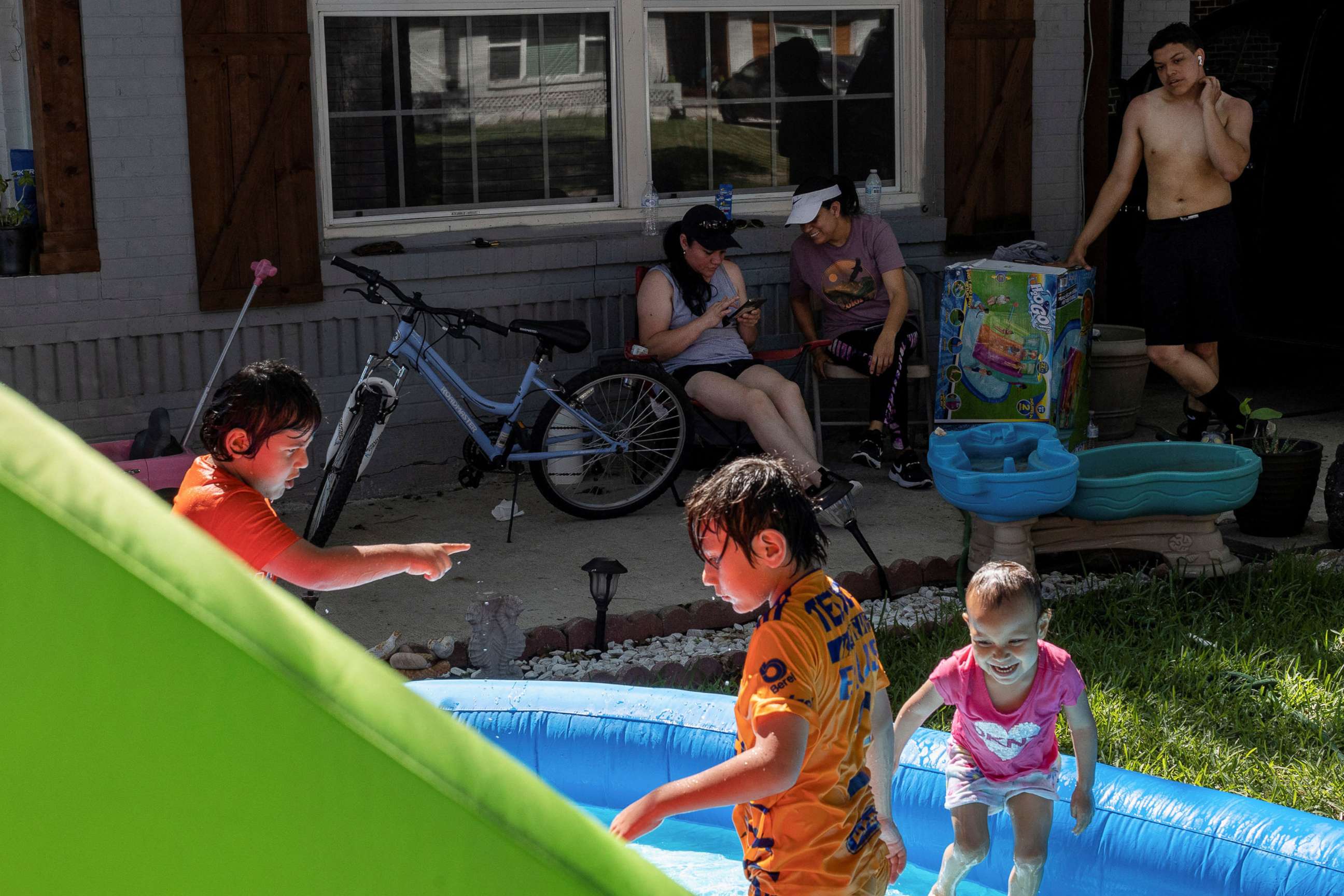 PHOTO: Neighbors Maria Hernandez, Luisa Ortega and Issac Montelongo sit outside as they watch the kids play in water during a heatwave with expected temperatures of 102 F in Dallas, June 12, 2022. 