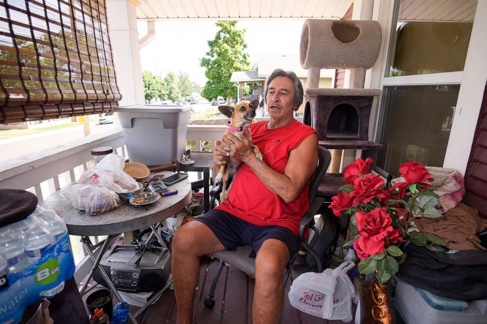 PHOTO: Ben Gallegos sits on the porch of his family's home with his dog as the daytime high temperature soars toward triple digits, July 27, 2023, in north Denver.