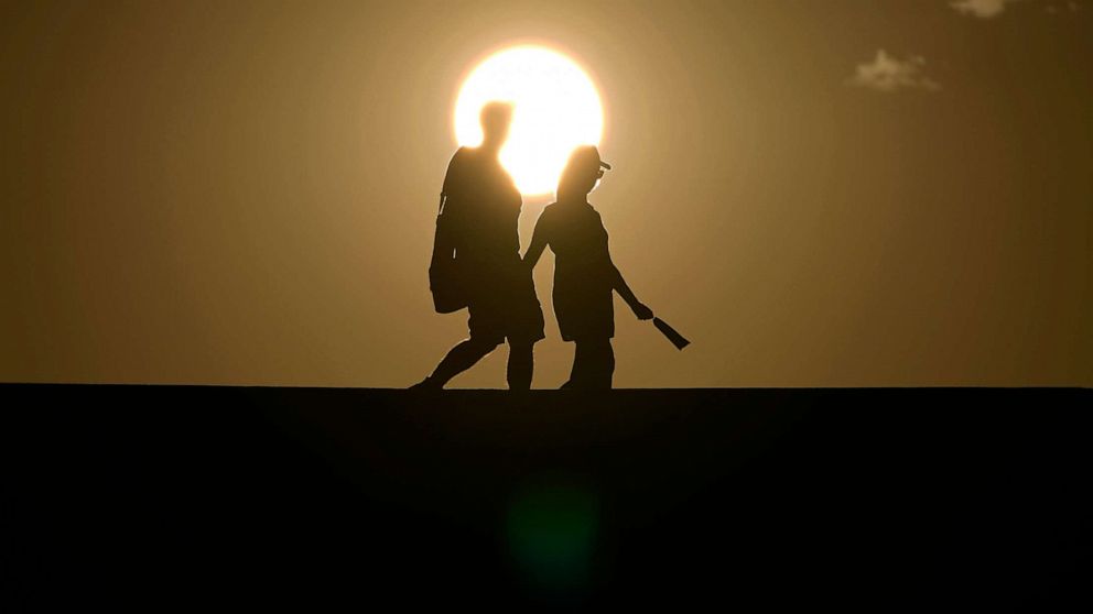PHOTO: People walk along a trail as the sun sets, July 16, 2023, in Death Valley National Park, Calif.