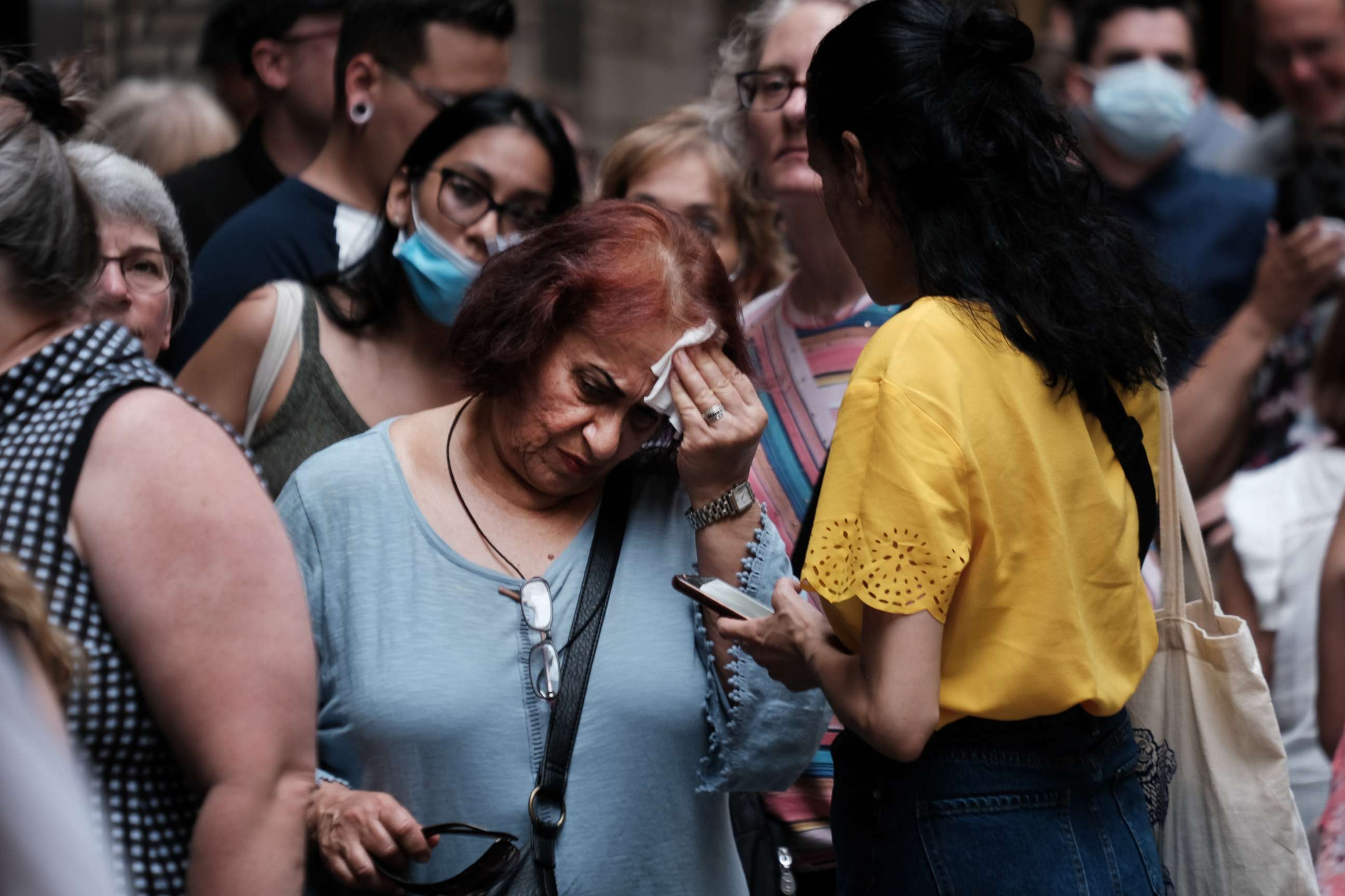 PHOTO: A woman wipes her brow as people wait in line to see Phantom of the Opera in midtown Manhattan as temperatures reach into the 90s on July 21, 2022, in New York City.
