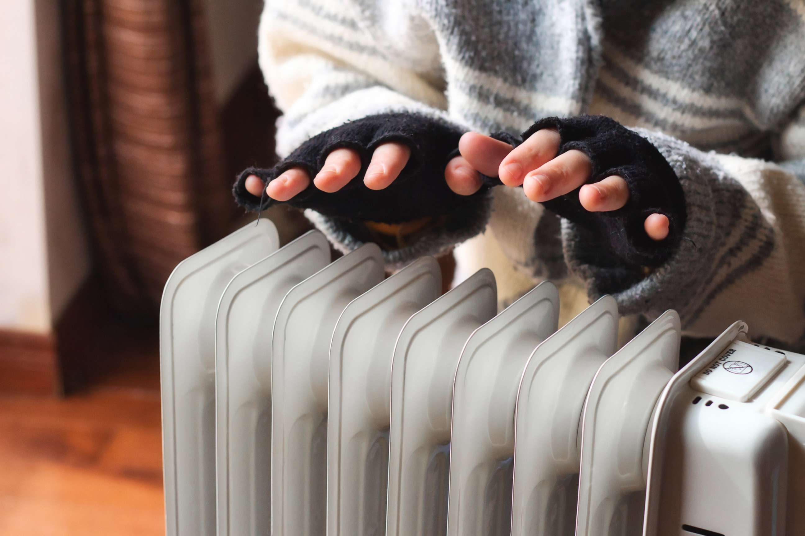 PHOTO: Person heating their hands at home over a domestic portable radiator in winter