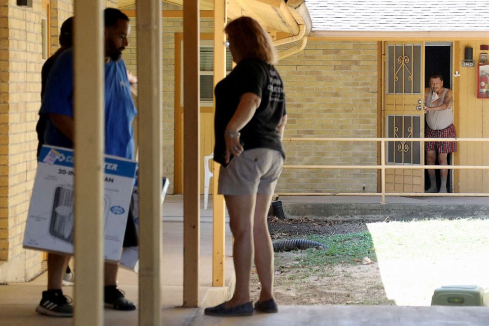 PHOTO: Ramiro Cervantes, right, peeks out his door to request a fan as a non-profit outreach group  delivers fans to residents in need of help coping with the heat in San Antonio, Texas, July 11, 2022.