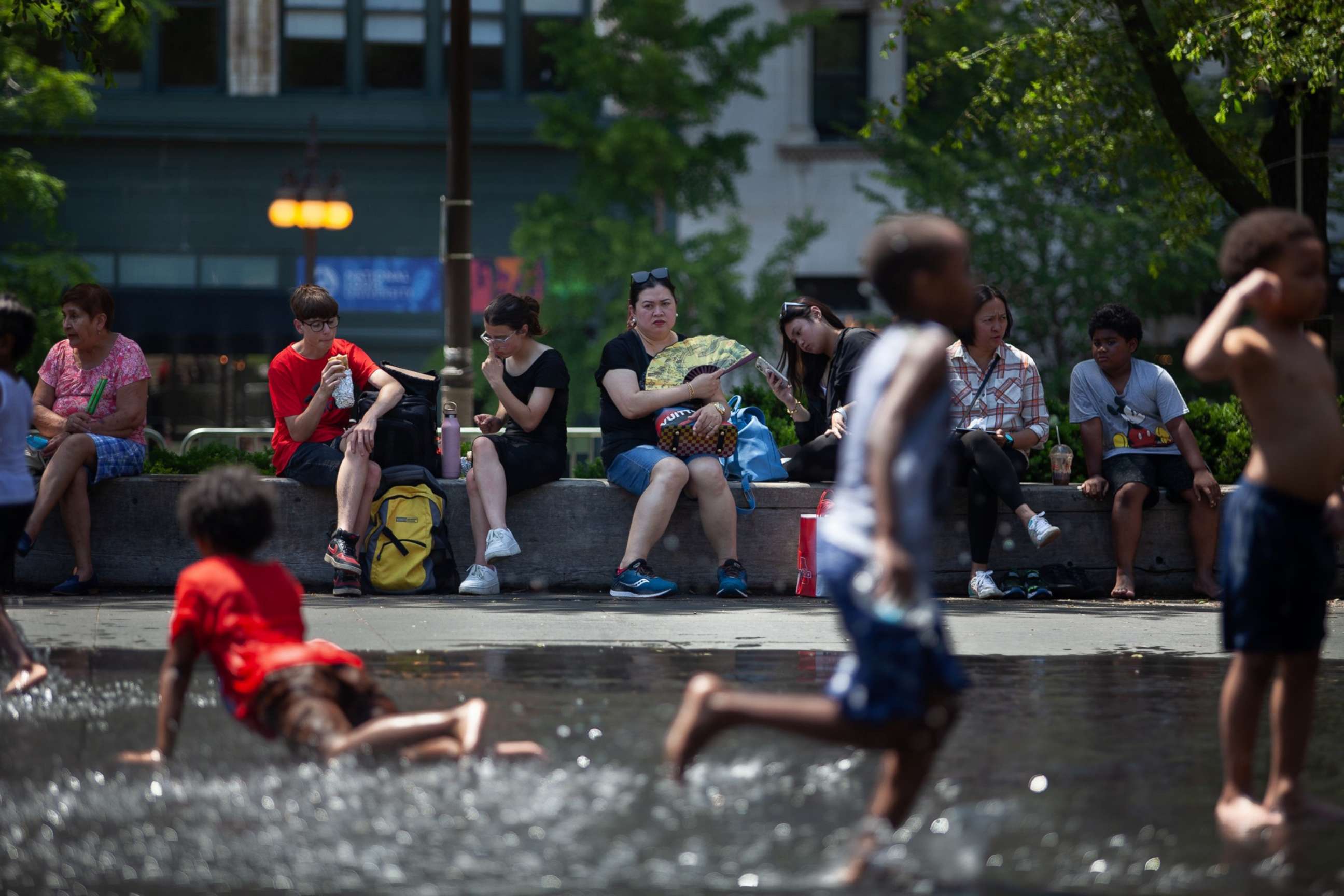 PHOTO: People sit in the shade as children play with water in downtown Chicago, June 14, 2022.