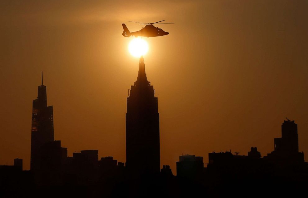 PHOTO: The sun rises behind the Empire State Building as a United States Coast Guard helicopter flies past at the start of another very warm day in New York City on May 22, 2022, as seen from Hoboken, N.J., May 22, 2022. 