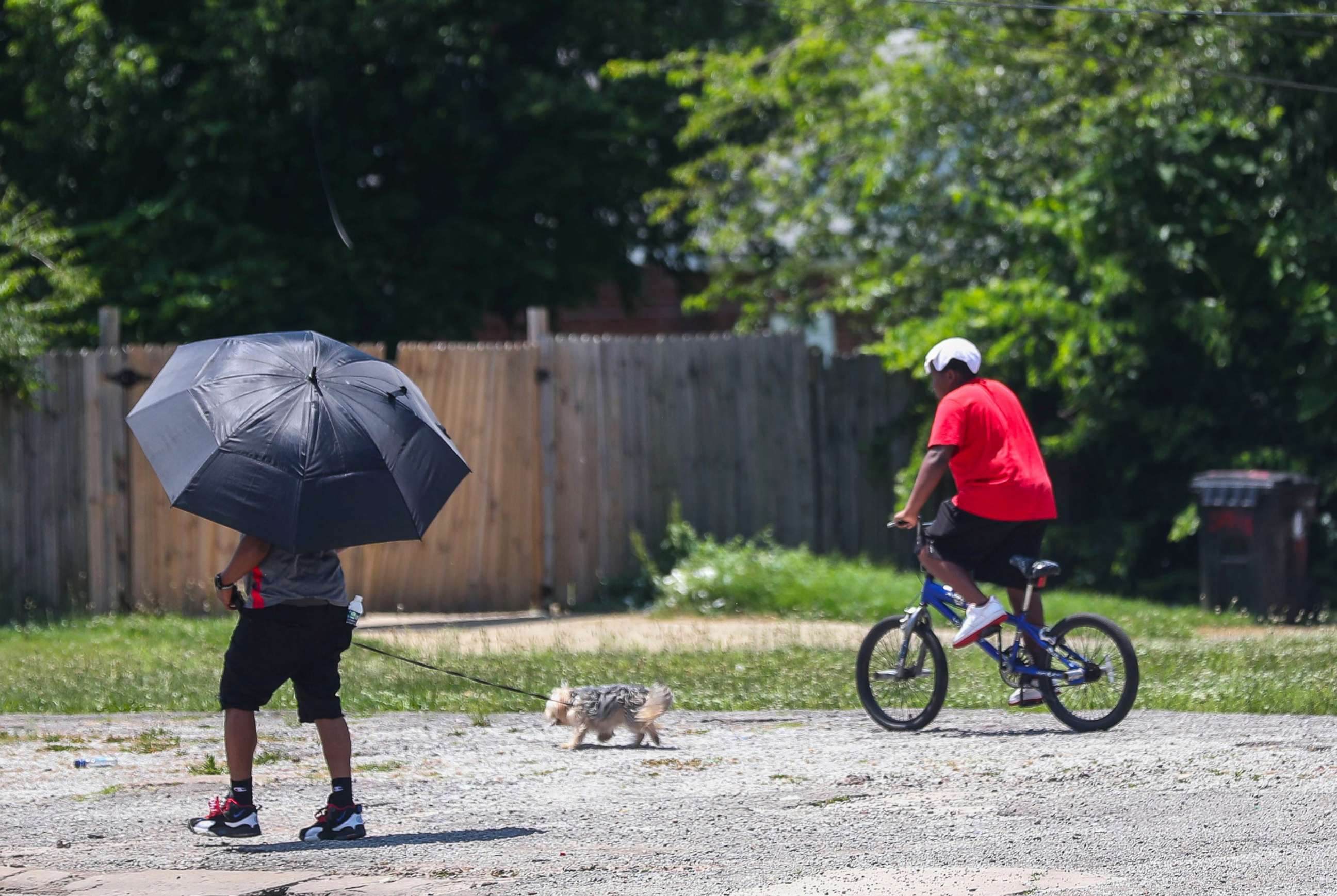 PHOTO: A pedestrian seeks shade under an umbrella as a rider bicycle keeps a wet cloth on his head while the pair head south on 34th Street in the Shawnee neighborhood of Louisville, Ky., June 14, 2022. 