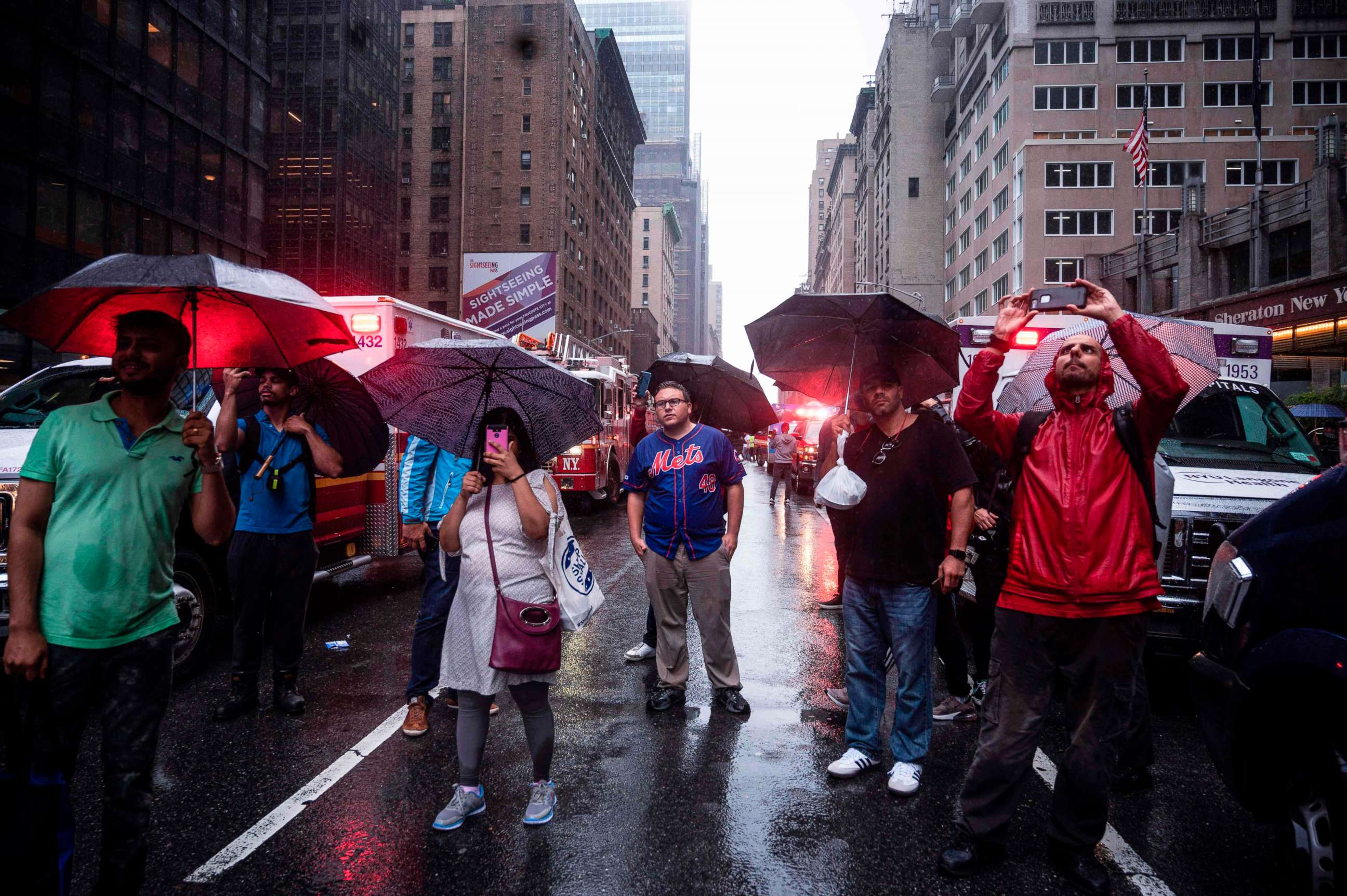 PHOTO: Onlookers take pictures on 7th  Avenue after a helicopter crash-landed on top of a building in New York, June 10, 2019. 