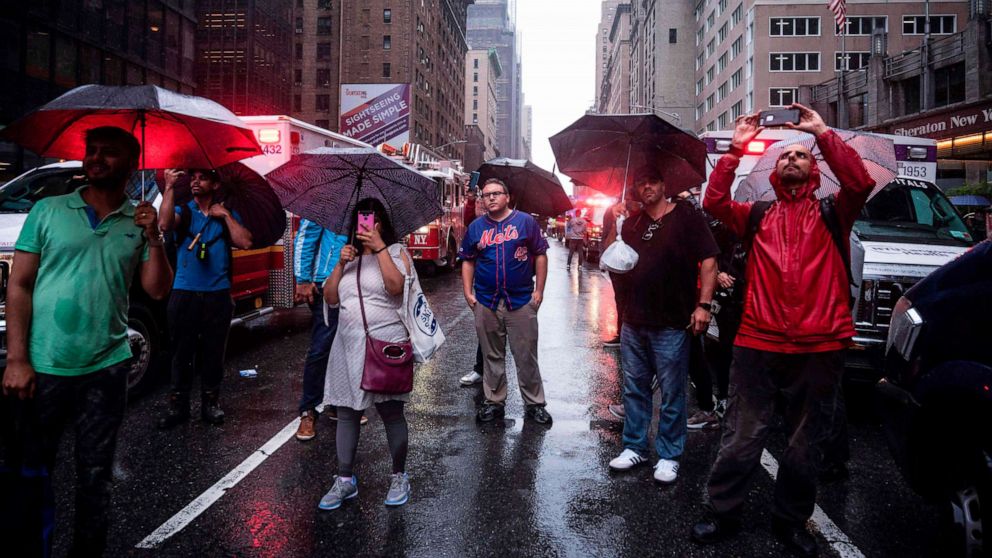 PHOTO: Onlookers take pictures on 7th  Avenue after a helicopter crash-landed on top of a building in New York, June 10, 2019. 