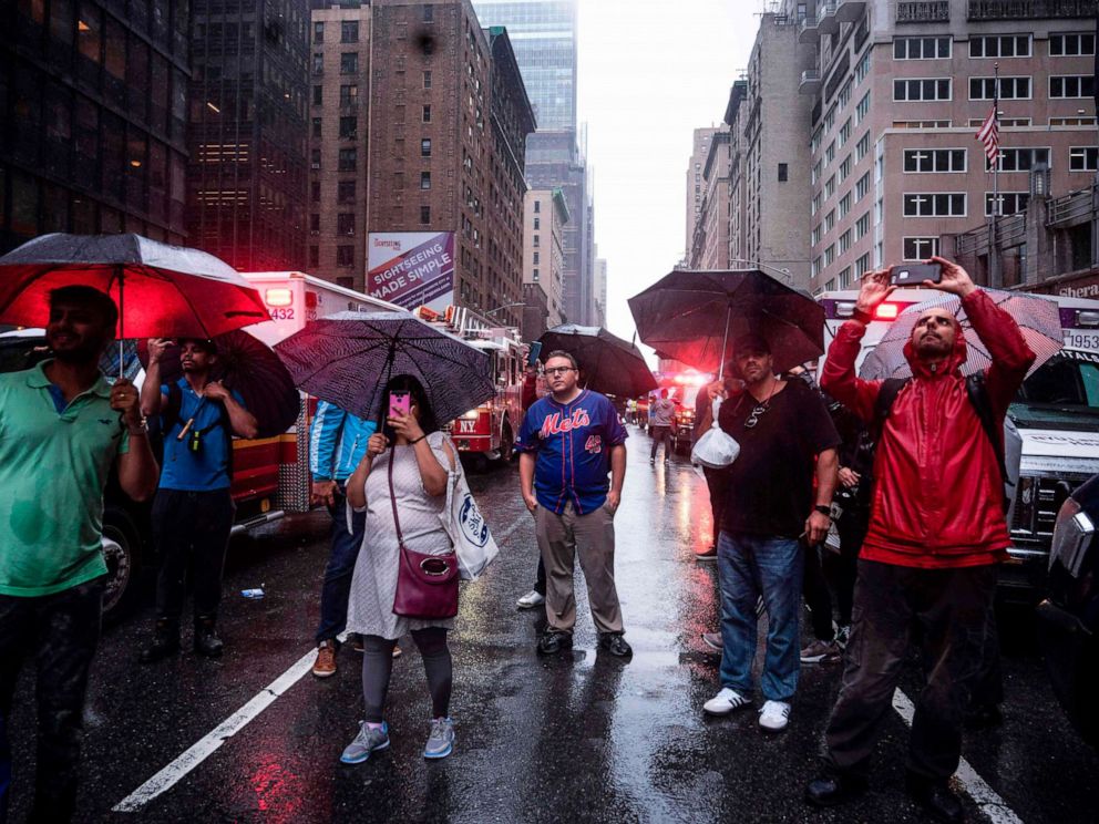 PHOTO: Onlookers take pictures on 7th Avenue after a helicopter crash-landed on top of a building in New York, June 10, 2019.