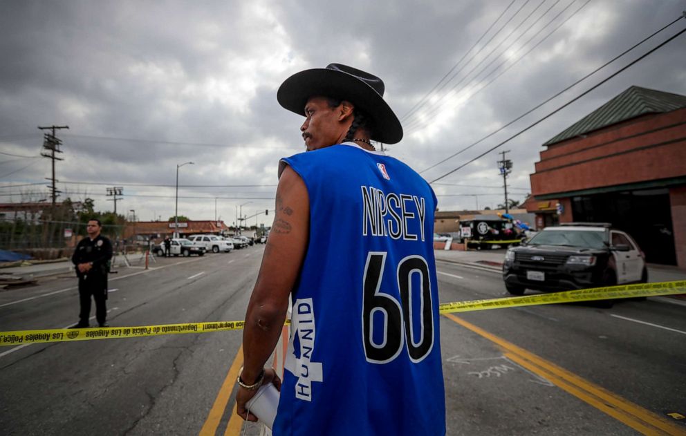 PHOTO: Herman "Cowboy" Douglas, business partner of Nipsey Hussle, stands behind police crime scene tape to pay his respect at a makeshift memorial for Hussle outside their clothing store, April 2, 2019, in Los Angeles. 