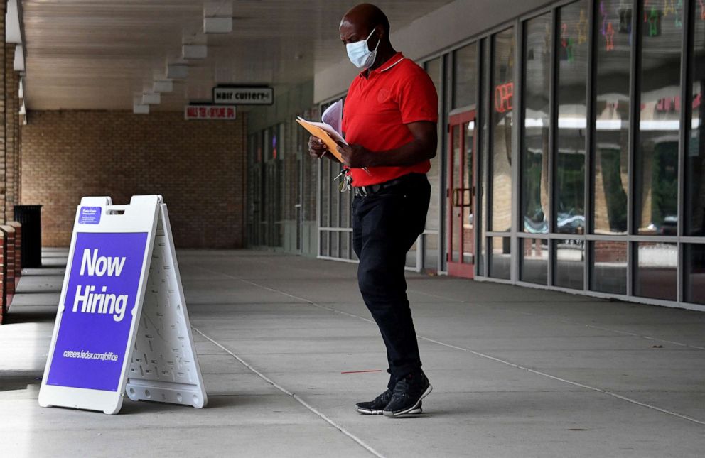 PHOTO: Pedestrians walk by a "Now Hiring" sign outside a store on August 16, 2021 in Arlington, Virginia.