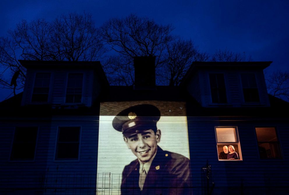 PHOTO: An image of veteran Emilio DiPalma, is projected onto the home of his daughter, Emily Aho, left, as she looks out a window with her husband, George, in Jaffrey, N.H., April 30, 2020.