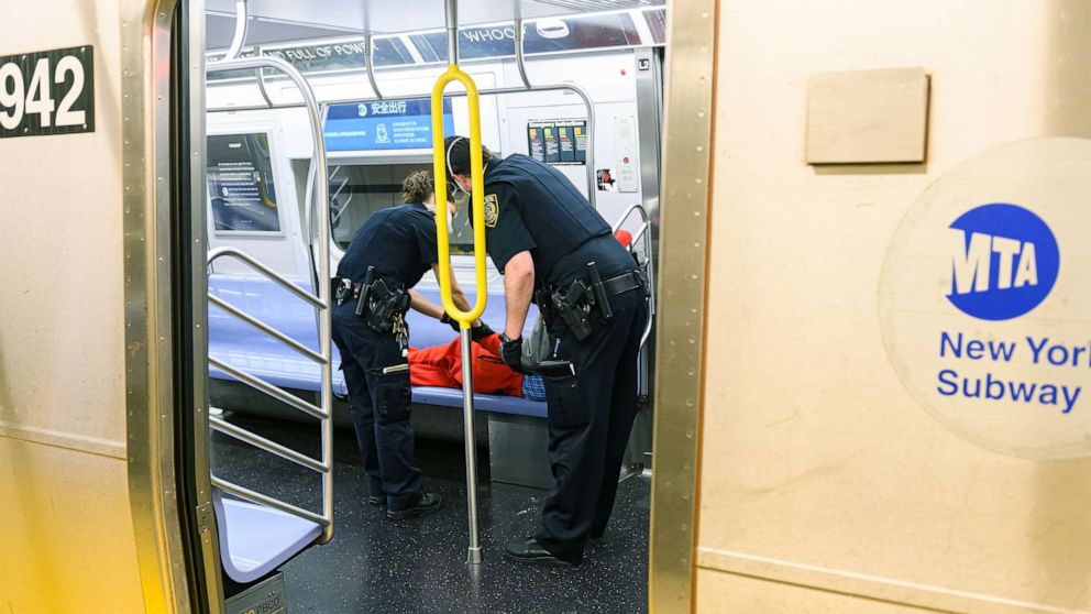 PHOTO: New York Police officers escort a sleeping person on the train, May 23, 2020, in New York.